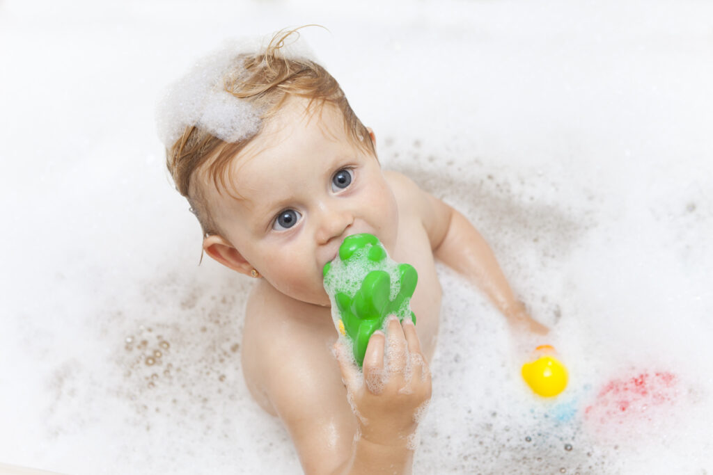 A baby in a bathtub with soap foam playing with rubber toys.