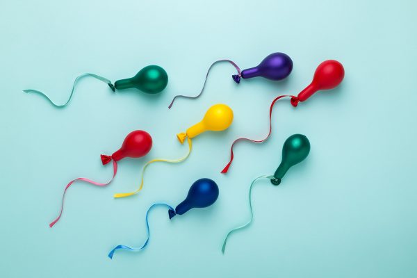 Colorful balloons in spermatozoid shape on blue. Trendy bright colors, minimal style. Sperm motion, donation concept. Abstract flat lay.